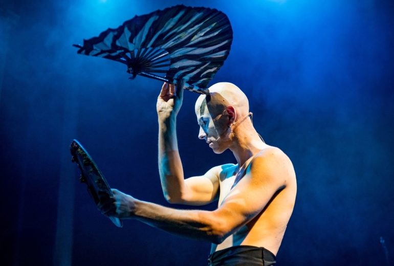 lithe man's torso dancing with a black fan against a blue backdrop. Power and art.